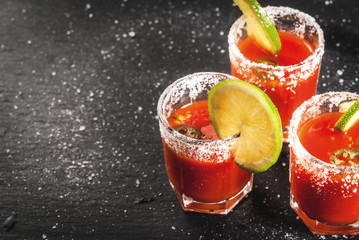 Mexican traditional alcohol drink. Sangrita, with tequila, tomato juice, hot spices, chili and lime.Analogous bloody mary. On black slate table, copy space