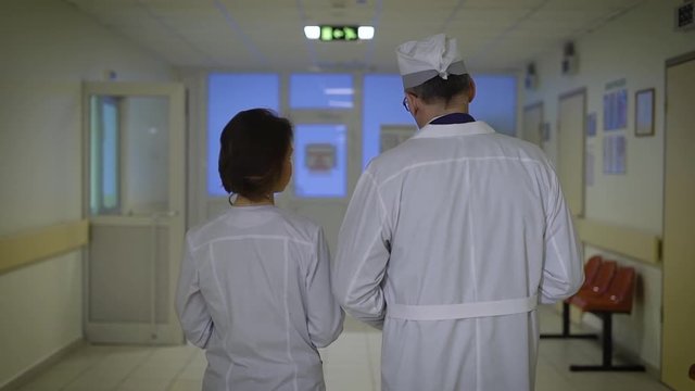 Doctors, a man and a woman go on a hospital corridor and communicate with each other. Medical workers keep a folder with the history of patients, and X-rays.