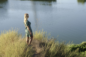 Young woman stands on the river bank and looks at the water