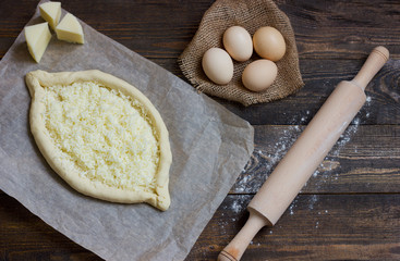 Khachapuri with eggs on sackcloth, flour, eggs and rolling pin on black table