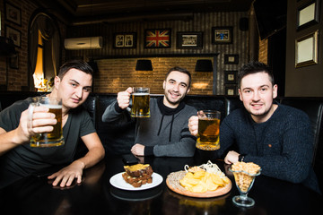 Young friends men with beer in pub and cheers and eat snaks