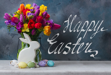 Spring fresh flowers with easter eggs and white pocelane rabbit with happy easter greetings on black background