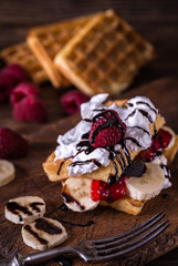 Belgian waffles with bananas and double cream on rustic table.