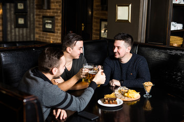 Three man friends drink beer and eat in traditional england pub.