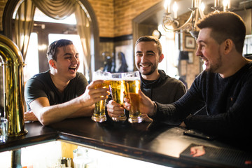 Friends in bar. Three happy young men in casual wear talking and drinking beer while sitting at the bar counter together