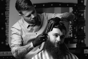 Handsome bearded man is looking forward while having his hair cut by hairdresser at the barbershop