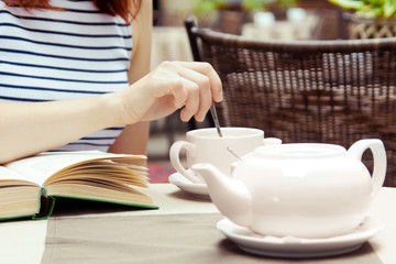beautiful young girl in outdoor cafe reading a book and drinking coffee.