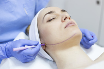Fototapeta premium Beautician draw correction lines on woman face. Woman in beauty salon