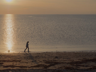 Fototapeta na wymiar Silhouette of a girl walking in water on a beach at dusk.