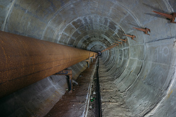 Old round dirty underground tunnel of heating duct with rusty pipeline