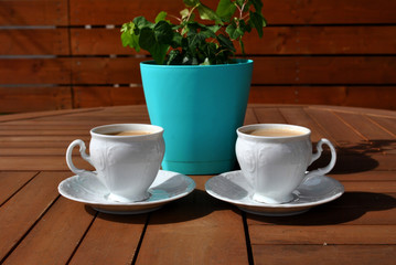 Two white cup of coffee and turquoise flower pot on wooden table