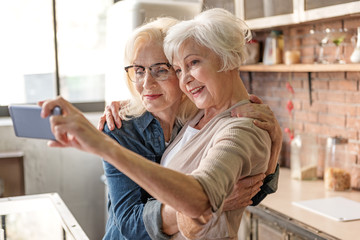 Cheerful old women making selfie in kitchen