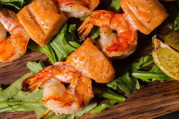 The shish kebab from shrimps and a salmon fried on coals with leaves of arugula and a lime