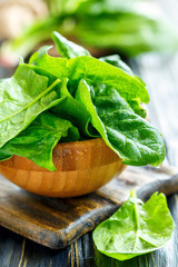 Wooden bowl with fresh spinach leaves in water drops.
