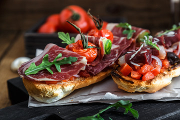 Close up bruschetta with proschuto, tomato, parmesan cheese and arugula