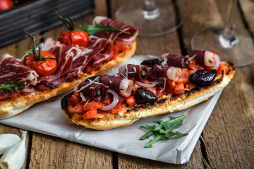 Wine appetizer set. Glass of red wine, brushettas with fresh tomato and jamon on over rustic grunge wooden background