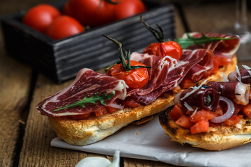 closeup shot of an bruschetta with tomatoes salsa, parma, arugula and olives, close view