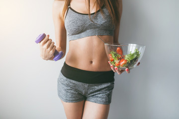 Girl holding salad and dumbbell after fitness training. - obrazy, fototapety, plakaty