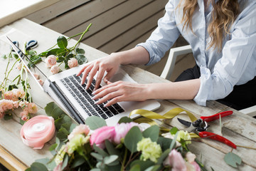 Smiling Mature Woman Florist Small Business Flower Shop Owner. She is using her telephone and laptop to take orders for her store. selective Focus.