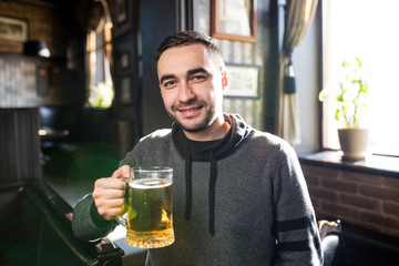 Handsome man in a pub or bar holding mug the beer high in the air for cheers
