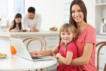 Fototapeta na wymiar Young woman and girl with laptop sitting at kitchen table