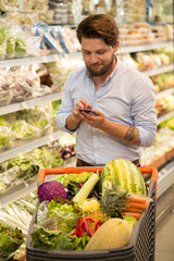 Young man using his phone at the supermarket