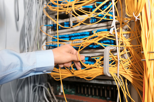 Hand of young engineer connecting cables in server room