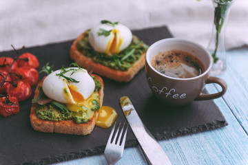 Breakfast with egg poached on avocado paddle and basil and a cup of coffee