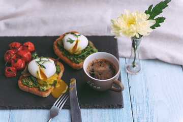 Breakfast with egg poached on avocado paddle and basil and a cup of coffee