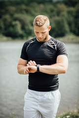 Fototapeta premium Runner standing at a pond checking time on his watch