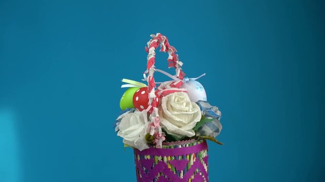 Rotating beautiful colorful Easter basket made from paper and eggs on blue background, 4K
