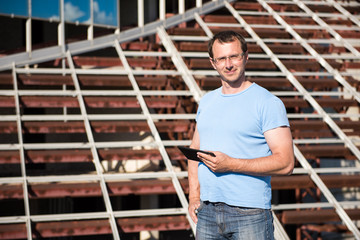 Young man with tablet stands on the background of building structures