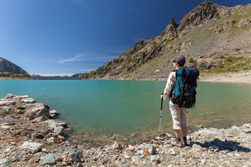Hiker woman with backpack on mountain lake in Italian Alps