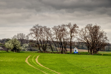 Fototapeta na wymiar Santa Barbara chapel landscape at spring, South Moravia, Czech Republic. Chapel in a field surrounded by trees with dramatic cloudy skies. High dynamic range.
