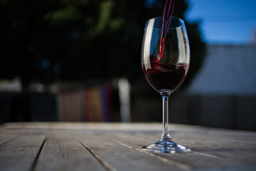 Close up image of wine being poured into a glass on a wooden table outside with natural light
