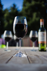 Close up image of wine being poured into a glass on a wooden table outside with natural light