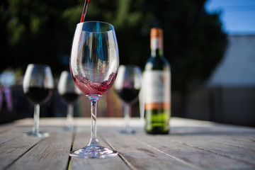 Close up image of wine being poured into a glass on a wooden table outside with natural light