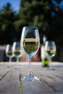 Close up image of white  wine being poured into a glass on a wooden table outside with natural light