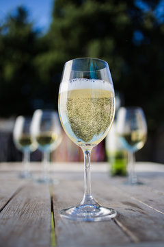 Close up image of white  wine being poured into a glass on a wooden table outside with natural light