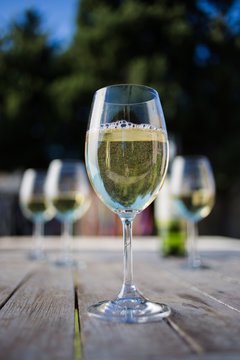 Close up image of white wine being poured into a glass on a wooden table outside with natural light