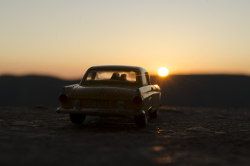 Fototapeta na wymiar silhouettes of Happy Couple sitting in old vintage car at sunset time. Toy installation effect like reality. Selective focus