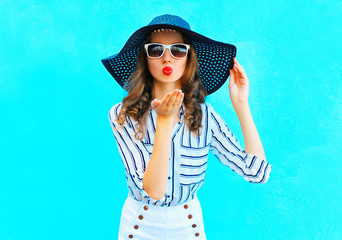 Fashion portrait pretty woman in straw summer hat is sends an air kiss over colorful blue background