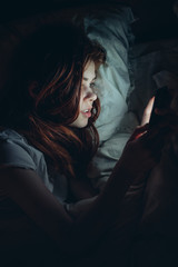 woman lies in bed and looks into phone