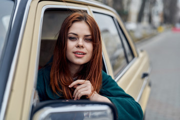 Fototapeta na wymiar confident red-haired woman peeking out of car window