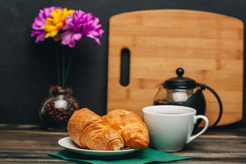 wooden board flowers in a jar croissants and a cup of tea on a table