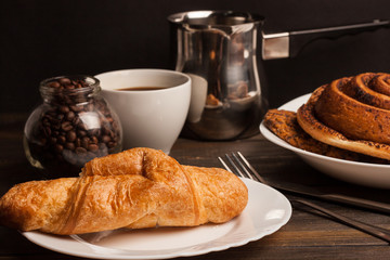 a jar with coffee beans croissants and a roll on plates, a ladle and a white cup