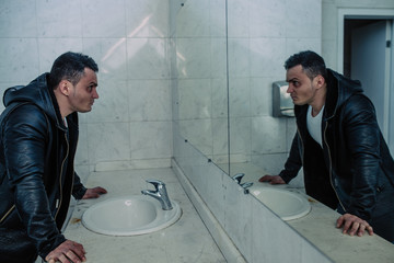 The wealthy man in expensive coat costs in a public toilet. He looks in a mirror and he has a...