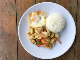 stir-fry vegetables with bean curd and shrimp in white dish with rice and fried egg on wooden background. Thai style Food.