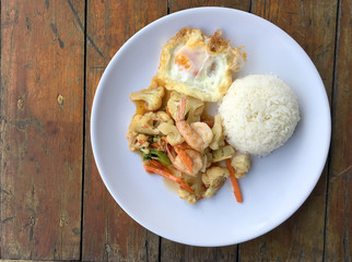 stir-fry vegetables with bean curd and shrimp in white dish with rice and fried egg on wooden background. Thai style Food.
