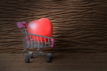 Still life painting photography with Stethoscope and red heart shape on mini shopping carts  on old beautiful wooden table, represents Love and Romance, World Heart Day